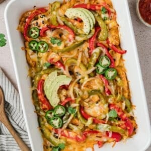 A baking dish filled with peppers, onions, chicken, and cheese.