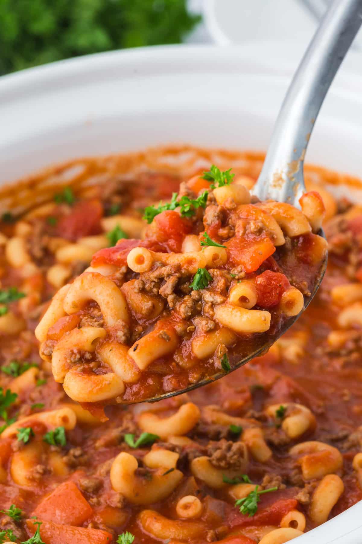 A spoonful of American goulash being lifted from a slow cooker.