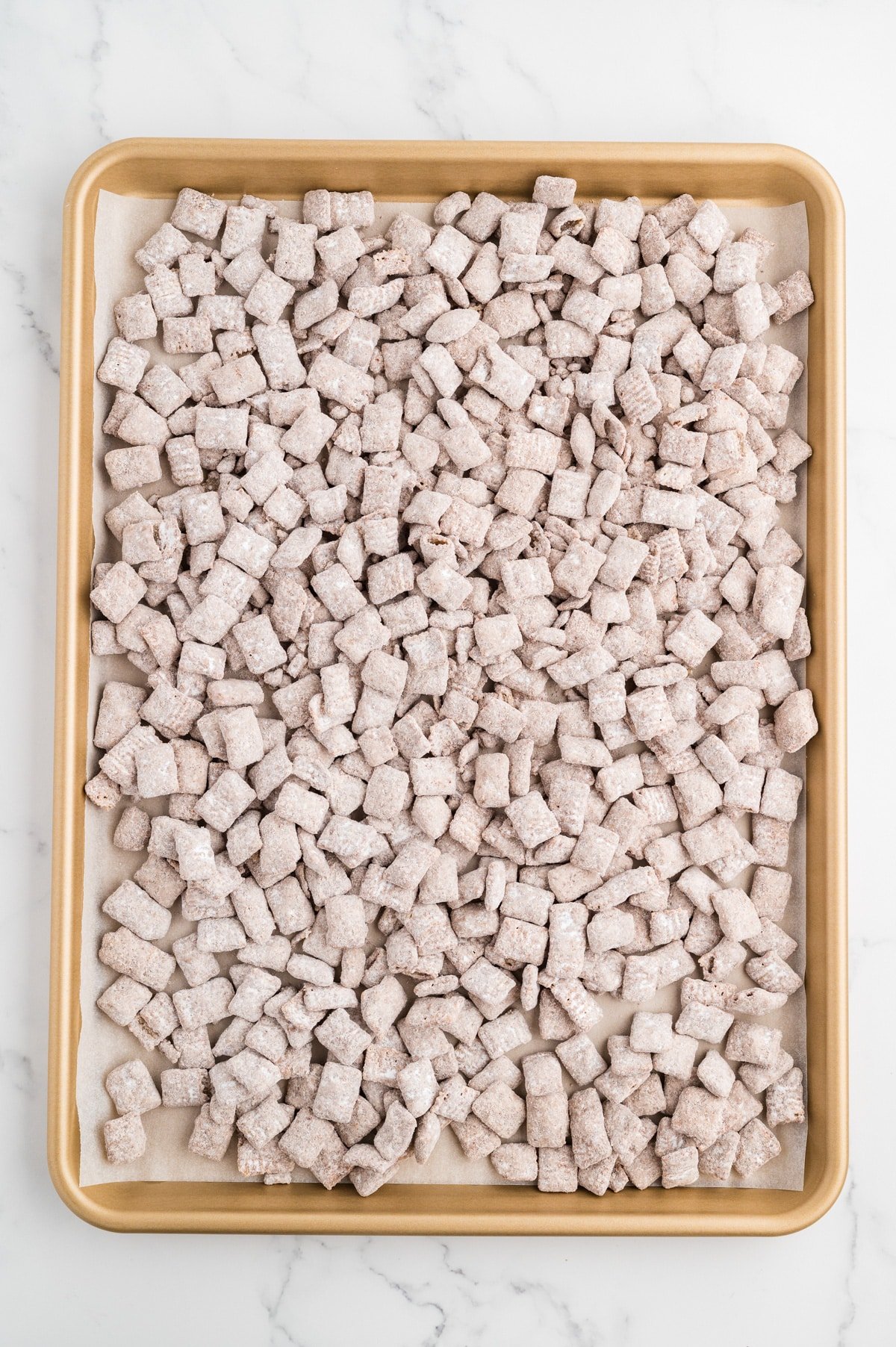 A sheet pan filled with homemade muddy buddies snack mix.