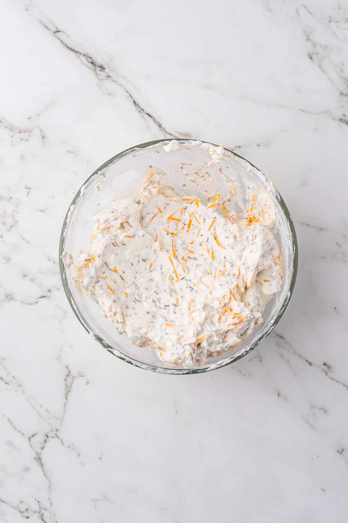 A bowl of cream cheese mixed with other ingredients, including cheese.