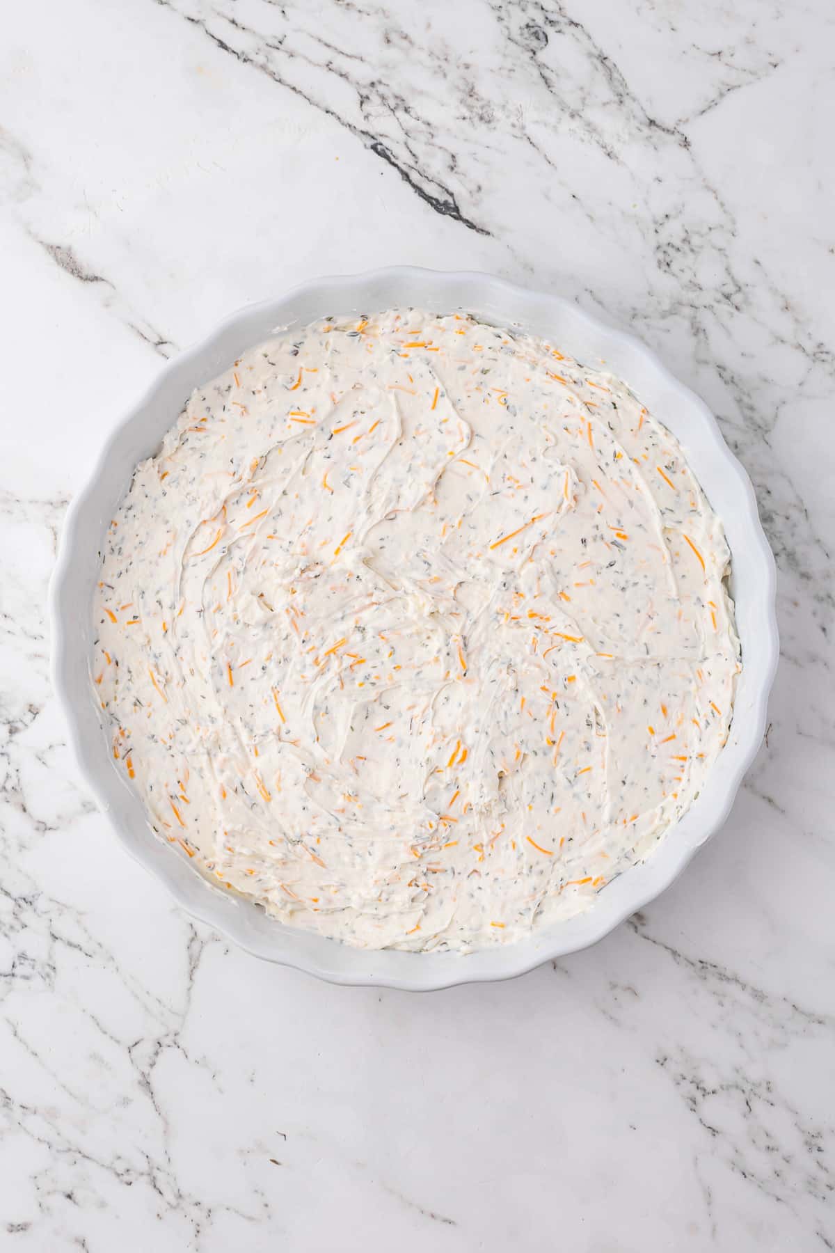 Cream cheese layered in the bottom of a round baking dish, dotted with cheddar cheese.