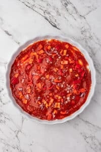 A baking dish with cream cheese, pizza sauce, and toppings layered.