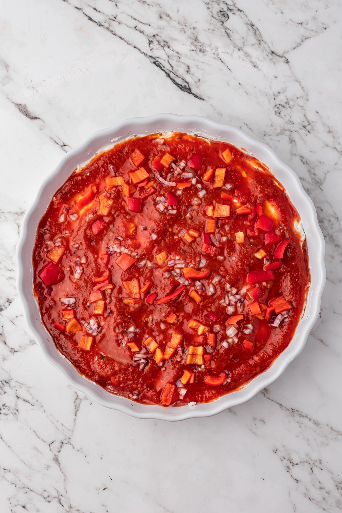 A baking dish with cream cheese, pizza sauce, and toppings layered.