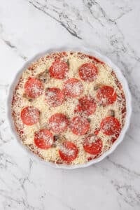 A round baking dish filled with layered dip, and topped with shredded cheese and pepperoni.