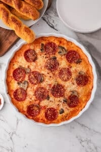 Bubbly and hot pizza dip in a round white baking dish, with garlic breadsticks on the side.