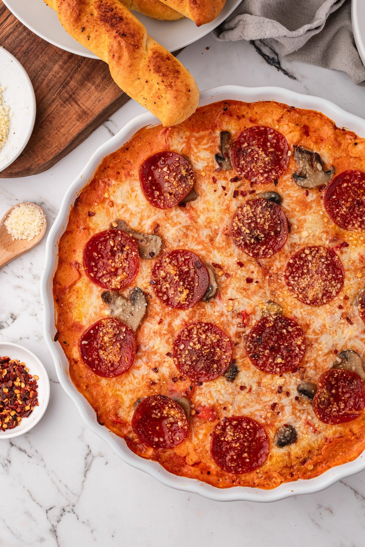 A bubbly baked pepperoni pizza dip, with breadsticks ready to dip in.