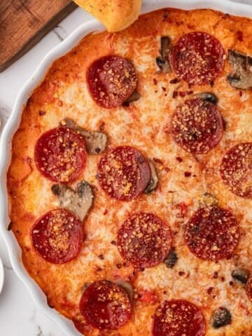 A bubbly baked pepperoni pizza dip, with breadsticks ready to dip in.