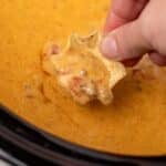 A tortilla chip dipping into a cheesy rotel dip in a slow cooker.