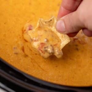 A tortilla chip dipping into a cheesy rotel dip in a slow cooker.