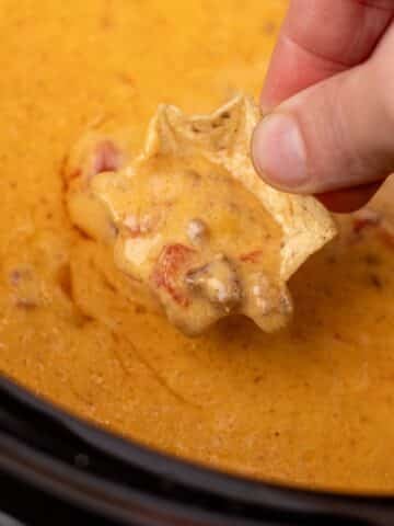 A tortilla chip dipping into a cheesy rotel dip in a slow cooker.