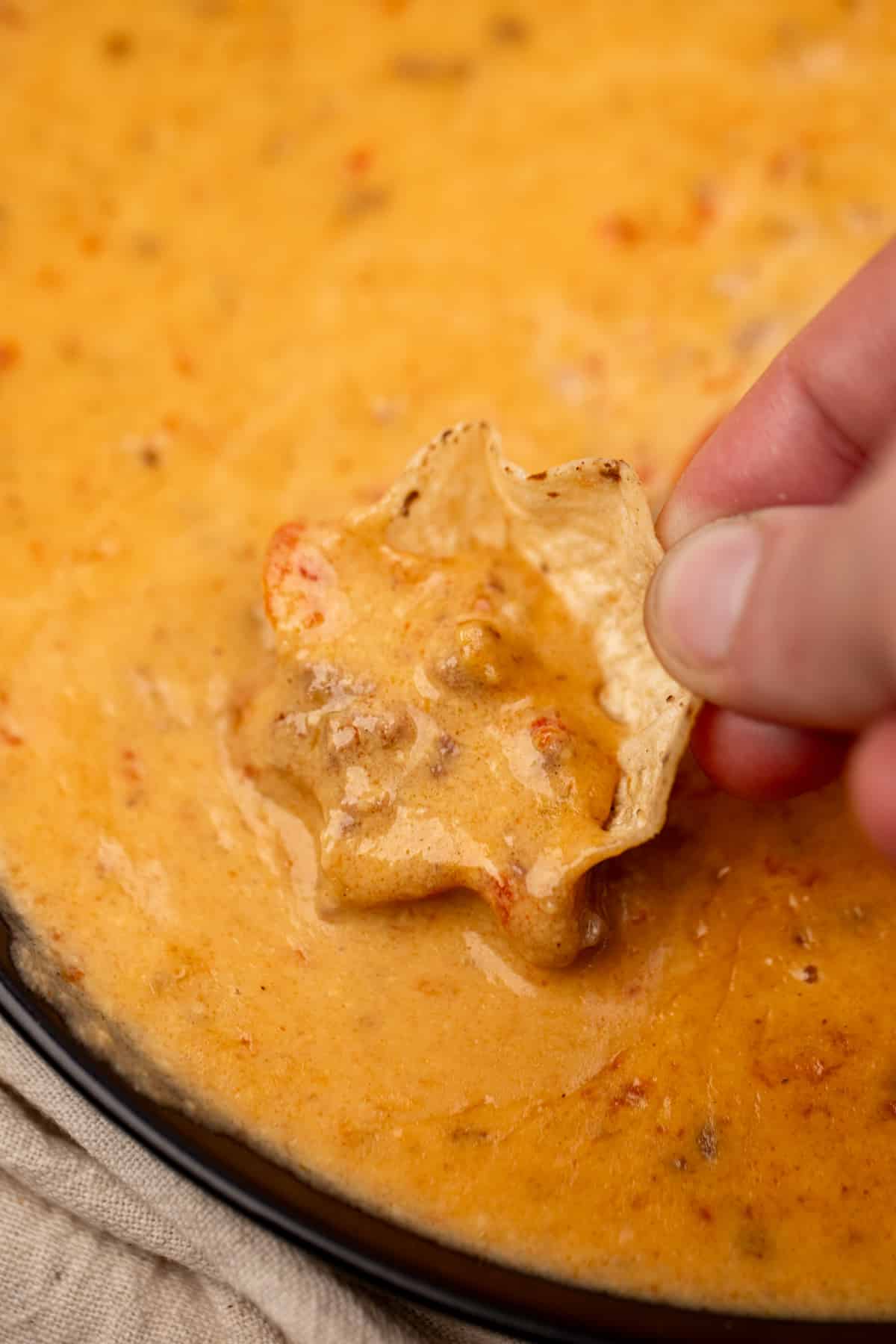 Dipping a chip into a cheesy ground beef dip.