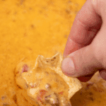 Dipping a tortilla chip into a slow cooker filled with melted rotel dip.
