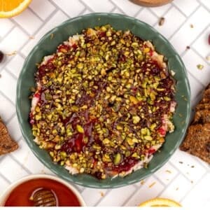 A bowl of boursin dip with cranberry sauce and pistachios.