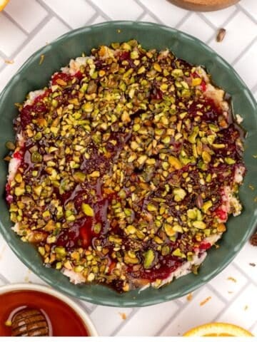A bowl of boursin dip with cranberry sauce and pistachios.