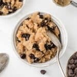 A small bowl of cookie dough filled with chocolate chips, and a spoon sticking out of the side.