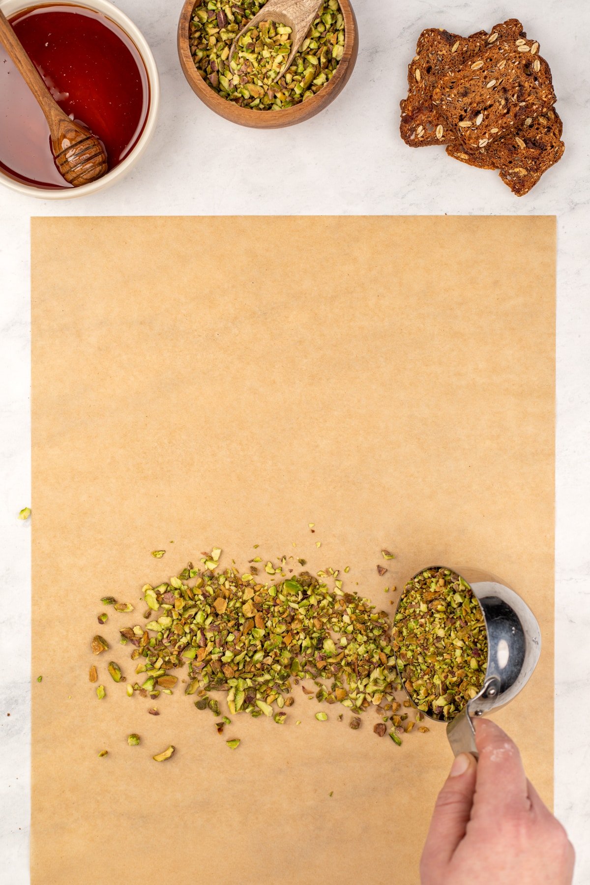 Pouring chopped pistachios on a sheet of parchment paper.
