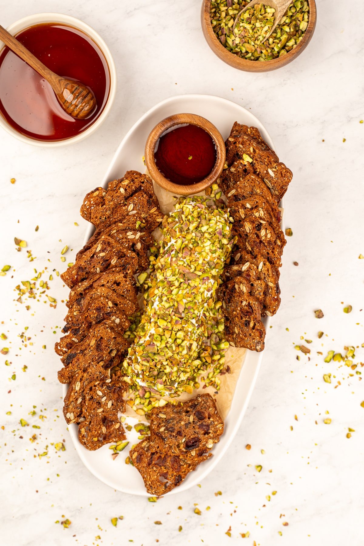 A platter with a rolled goat cheese log, fruit and nut crackers, and a small bowl of honey.
