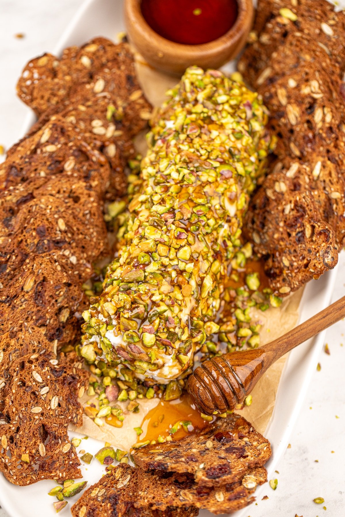A log of goat cheese coated in pistachios, with a honey dipper off to the side.