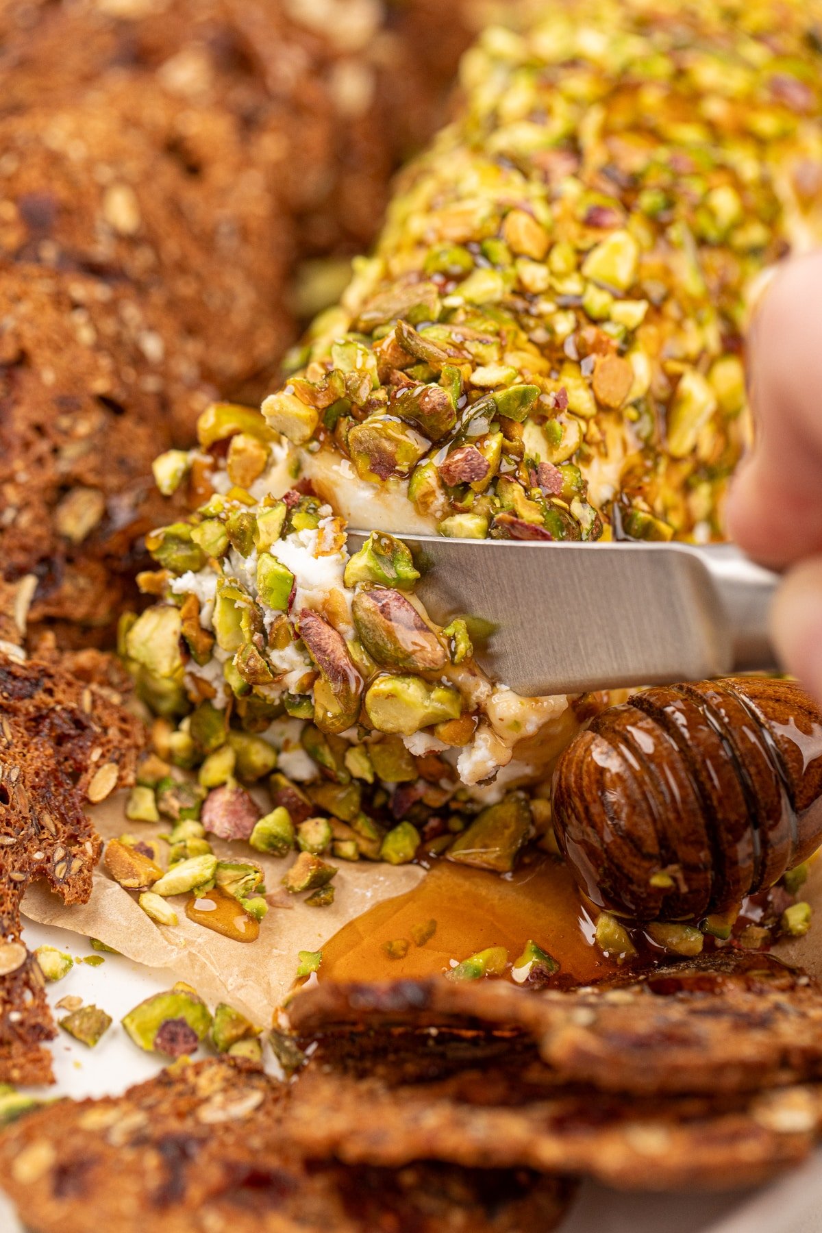 Using a dip spreader to slice into a pistachio coated cheese log.