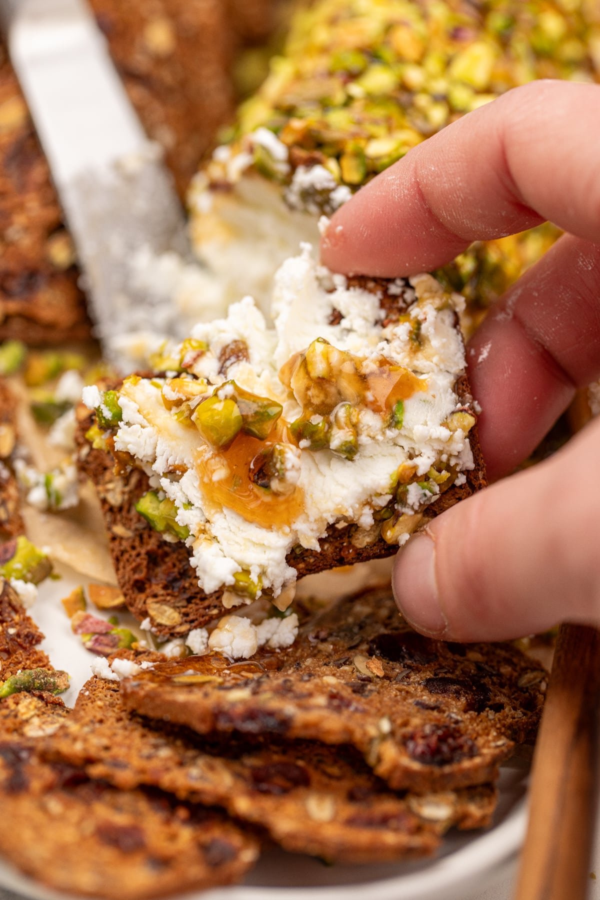 Goat cheese spread onto a charcuterie cracker, topped with pistachio and honey.