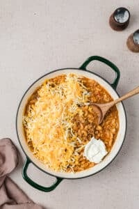 Adding cheese and cream cheese to a skillet with cooked macaroni.