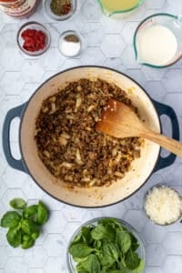Browned sausage in a Dutch oven with onion and garlic added.