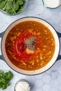 A dutch oven filled with broth, tomato sauce, tomato paste, and seasonings.