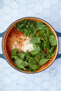 A dutch oven filled with soup, with spinach, basil, and parmesan added and ready to stir in.