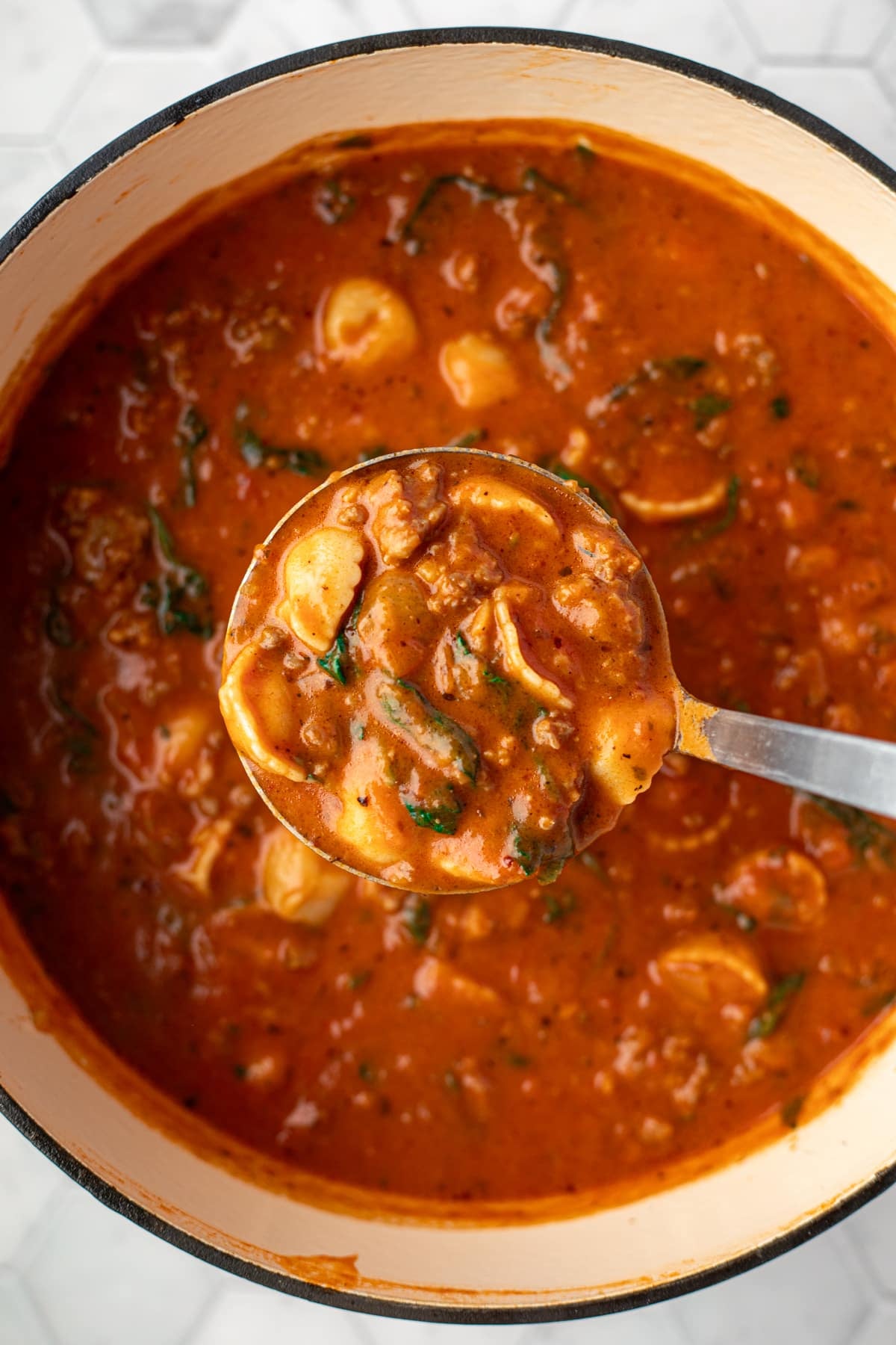 Taking a ladleful of tortellini and tomato soup from a Dutch oven.