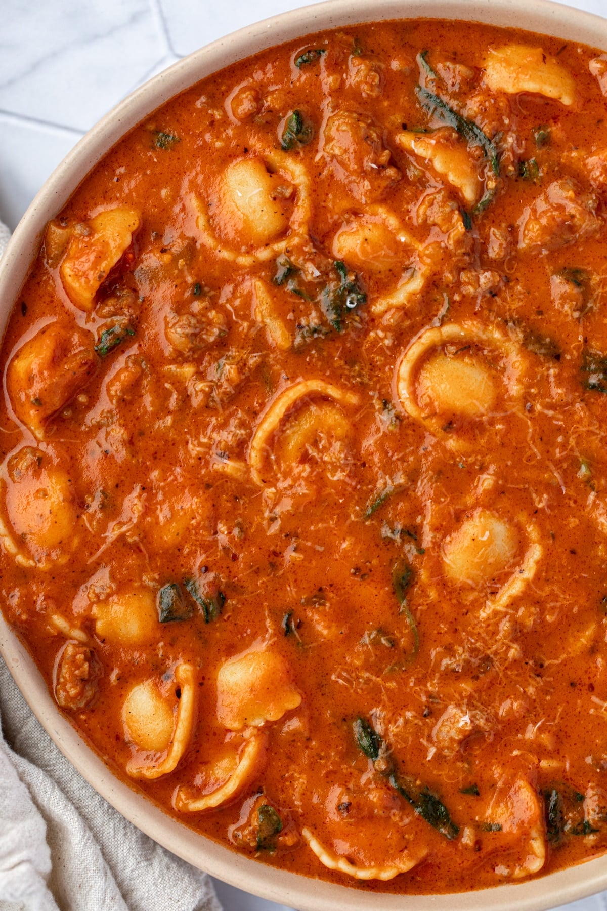 A bowl of tortellini and tomato soup filled with baby spinach.