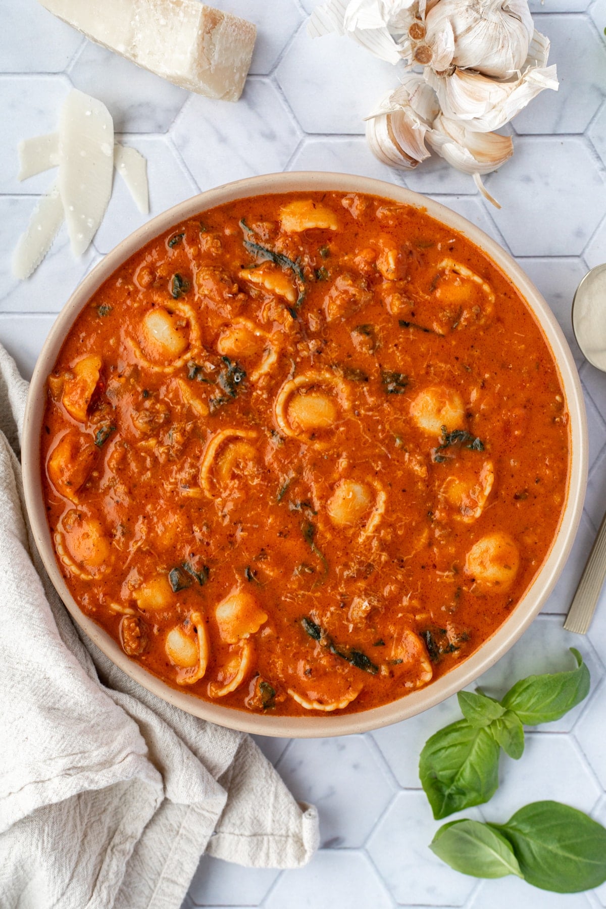 A bowl of tomato based tortellini soup garnished with fresh basil.
