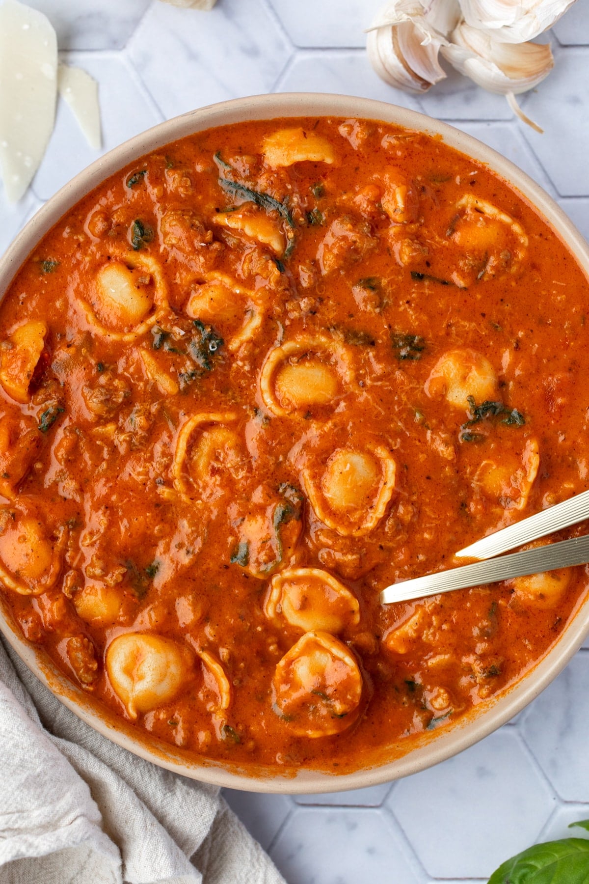 A bowl of tortellini soup with two spoons sticking out of the side.