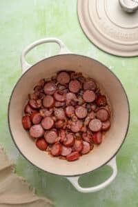 A Dutch Oven filled with smoked sausage and bacon.