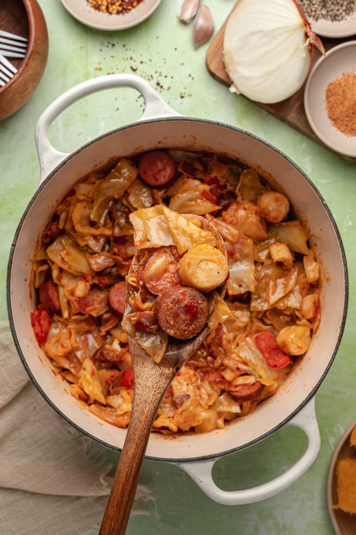 A wooden spoon taking a portion of cabbage and sausage from a Dutch oven.