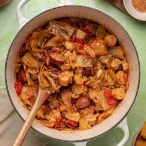 A Dutch oven filled with stewed cabbage, sausage, bacon, and hearts of palm.