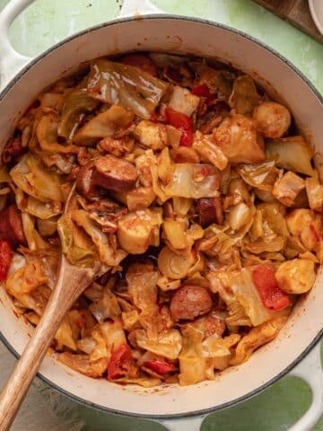 A Dutch oven filled with stewed cabbage, sausage, bacon, and hearts of palm.