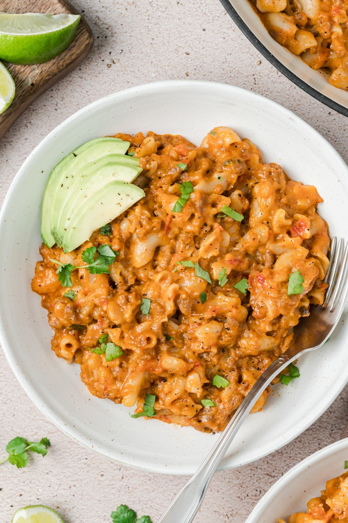 A bowl of taco mac garnished with avocado and cilantro.