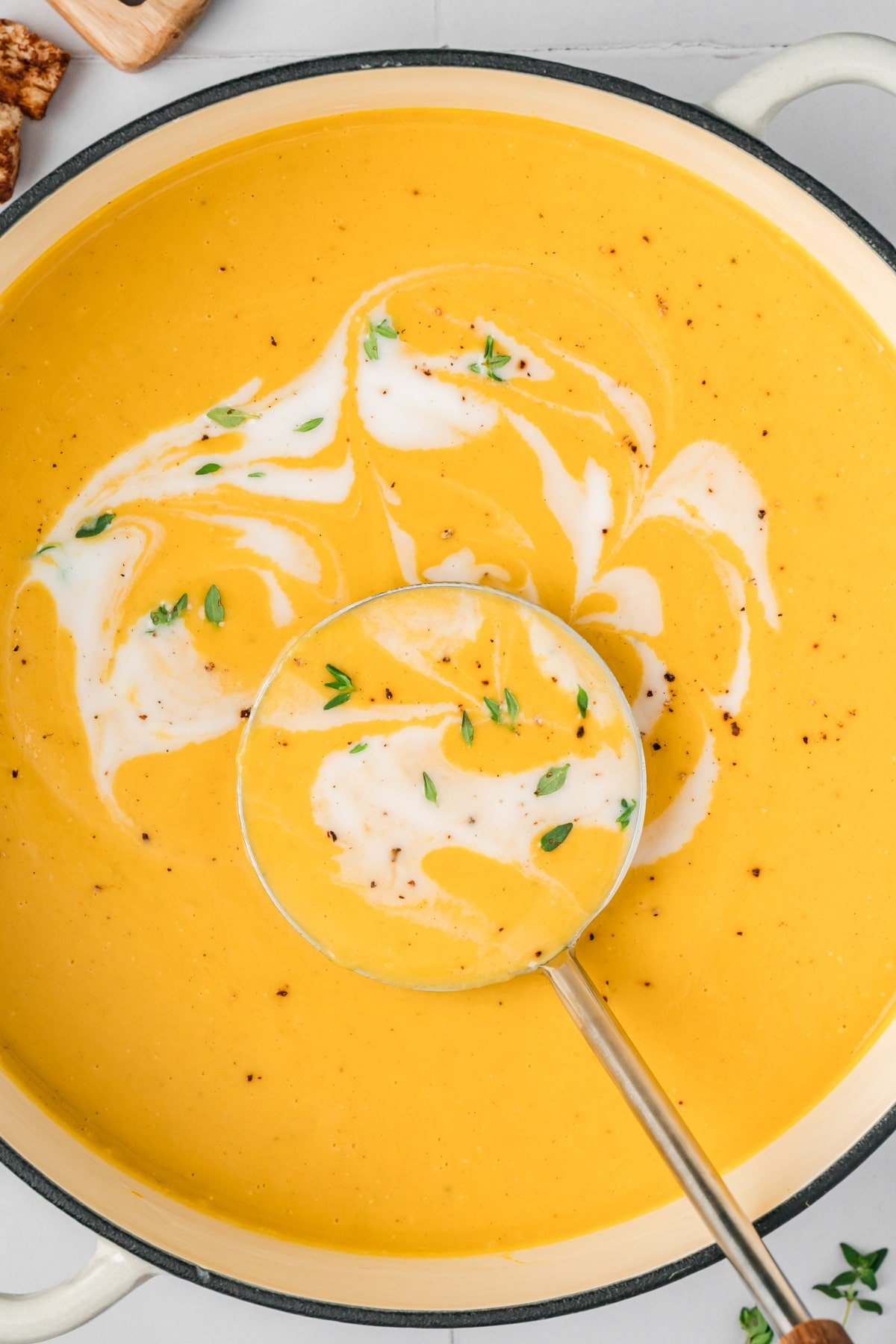 A Dutch oven filled with butternut squash soup, with a swirl of coconut milk in the center.