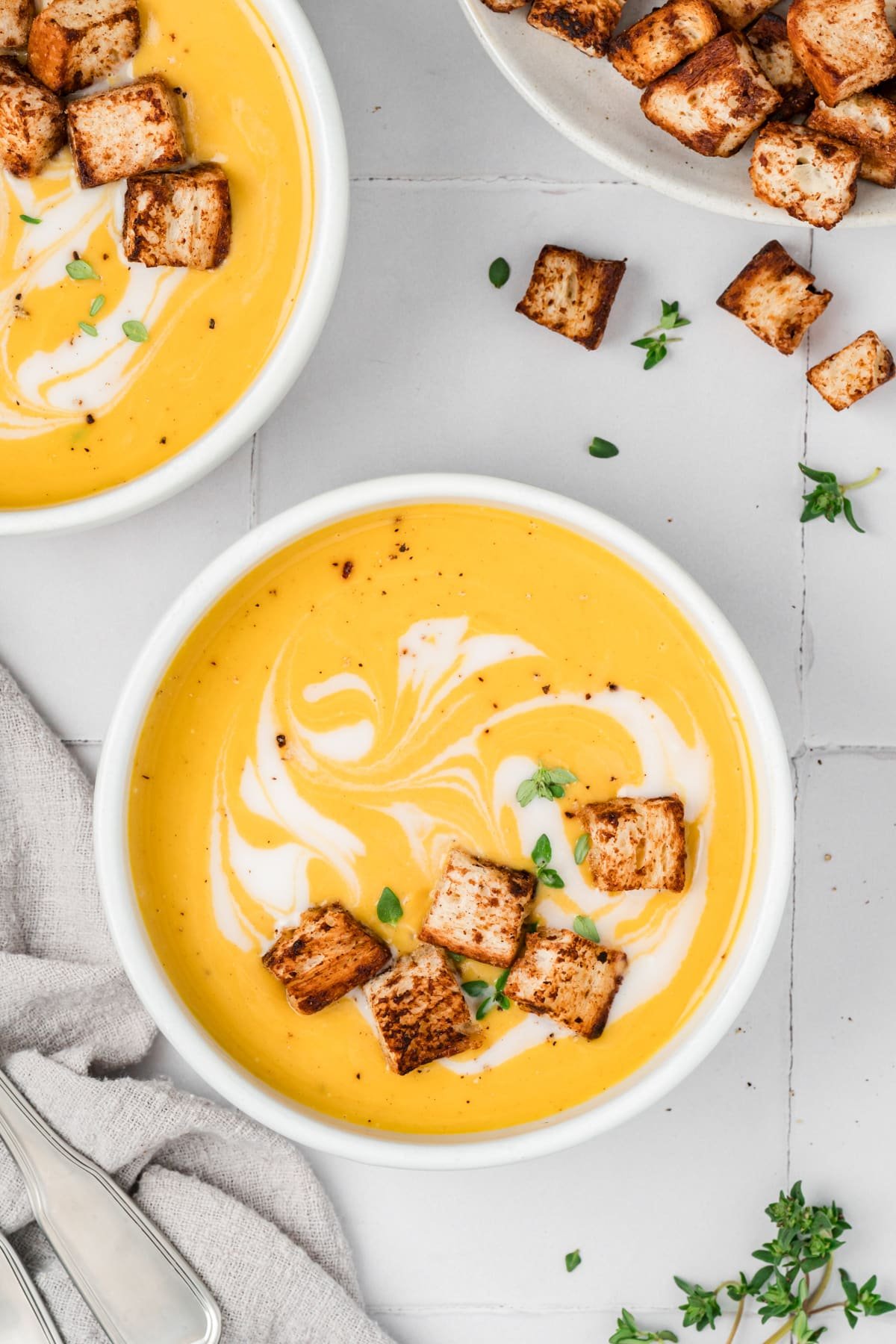 A bowl of butternut squash soup with a coconut milk swirl and some croutons floating on the top.