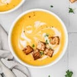 A bowl of butternut squash soup with croutons floating on the surface.