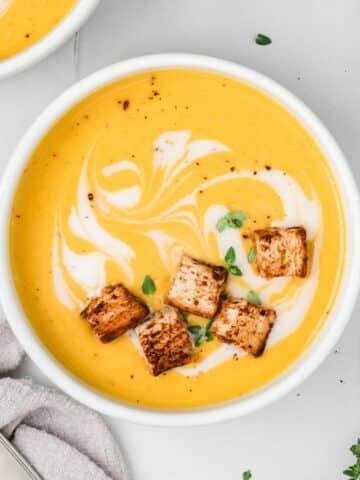 A bowl of butternut squash soup with croutons floating on the surface.