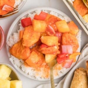 A bowl of rice with sweet and sour chicken on top.