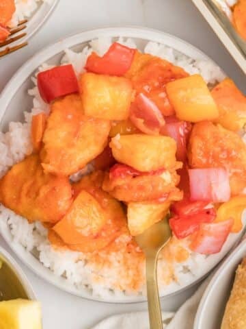 A bowl of rice with sweet and sour chicken on top.