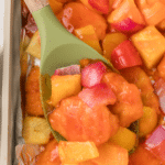 A spoon lifting a portion of sweet and sour chicken from a baking sheet.