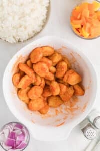 A bowl of chicken nuggets lightly coated in sweet and sour sauce.