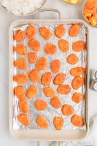 A foil-lined sheet pan with chicken nuggets spaced out evenly.