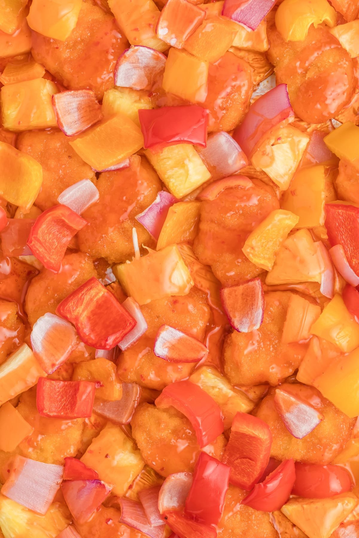 Chicken, pineapple, red onion, and bell peppers cooked in a shiny sauce on a sheet pan.
