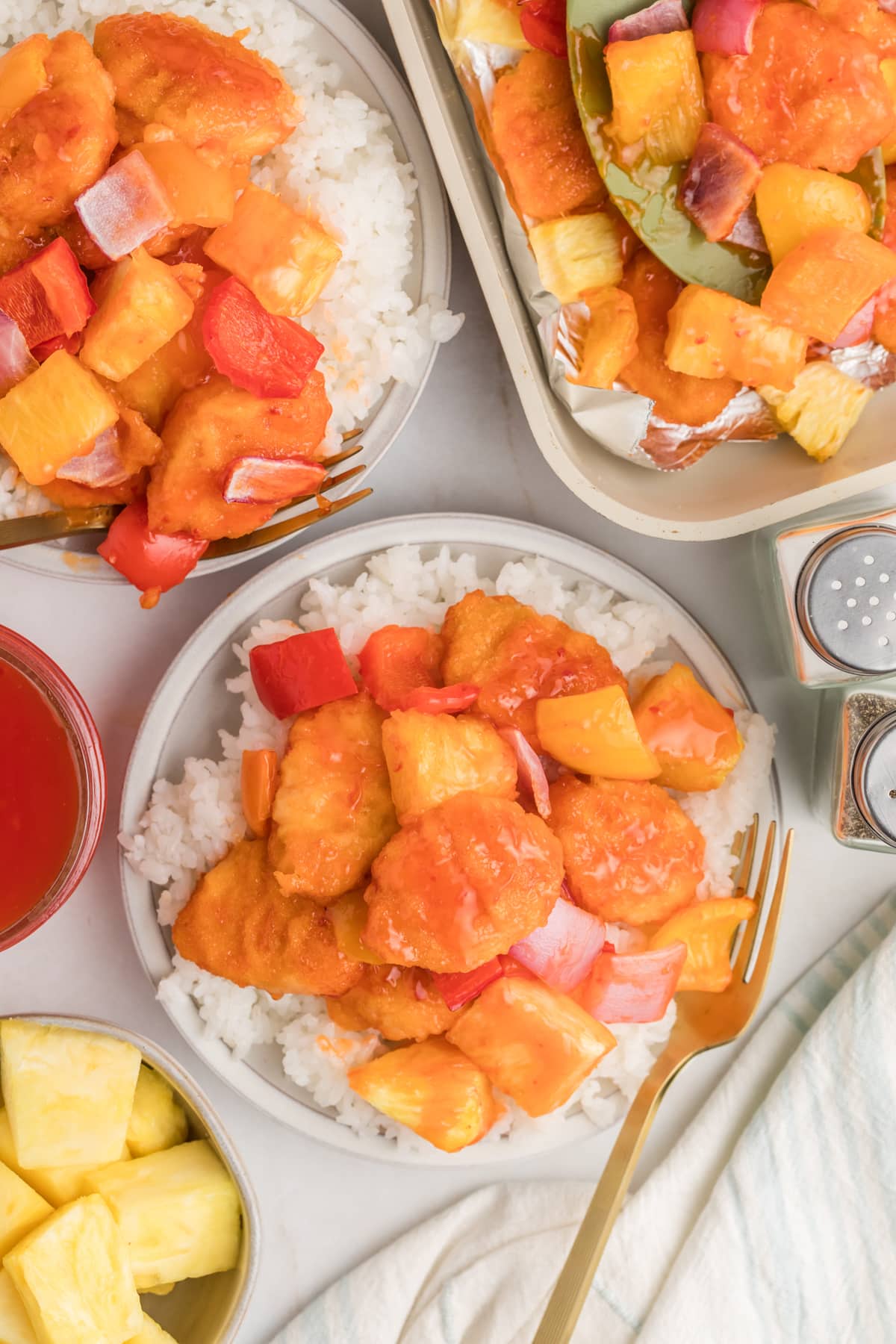 A bowl of cooked rice with sweet and sour chicken on top.