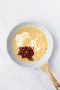 Adding cream and sundried tomatoes to a skillet to make a creamy sauce.