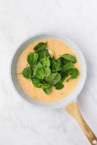 Adding spinach to a creamy sauce in a skillet.